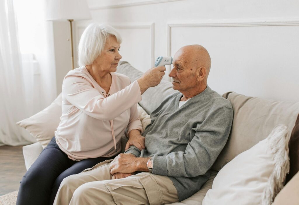 elderly parent's temperature being checked by caregiver to monitor for infection
